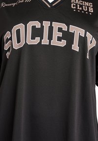 Schwarzer Stoff mit großen beigen Blockbuchstaben, die "SOCIETY" buchstabieren, und kleinerem weißen Text "Racing Club" in der Nähe des Ausschnitts.