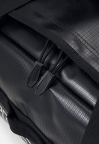 Intérieur d'un sac à dos noir avec une doublure texturée, deux verrous à cordon noirs et des sangles tissées, conçu pour une fermeture sécurisée et une fonctionnalité optimale.