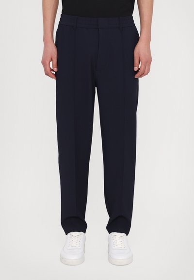 Pantaloni bleumarin dintr-un material neted, cu croială lejeră, față pliată și talie elastică, asortați cu adidași albi.