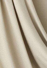 Gros plan sur un tissu beige avec des plis doux et une texture tissée fine et lisse.