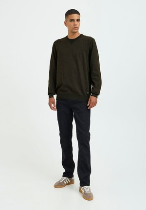 Donkergroene trui met lange mouwen en een ribgebreide ronde hals, gedragen met zwarte slim-fit broek en grijze sneakers met witte strepen.