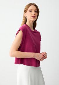 Top corto a maniche corte in tessuto magenta uniforme. Collo rotondo e vestibilità comoda, con una texture liscia e una leggera elasticità.