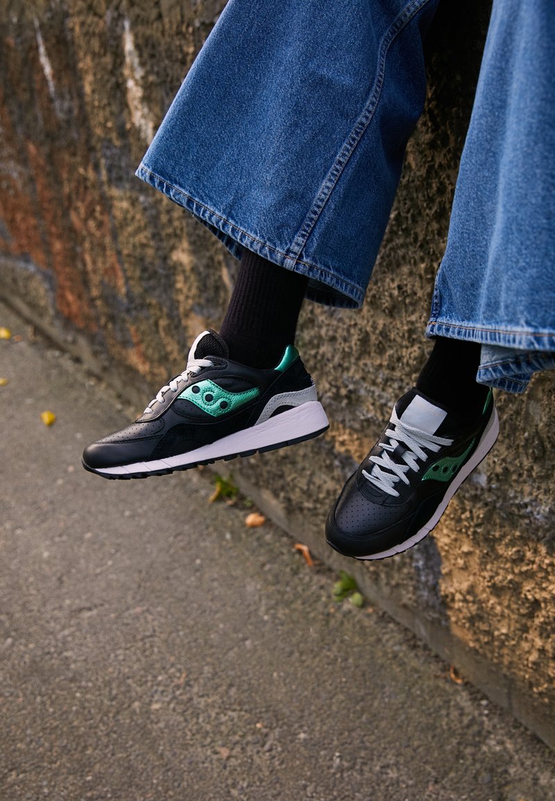Schwarze und grüne Sportschuhe mit durchbrochenem Detail, Schnürsenkel in Schwarz und Weiß, aus strukturiertem Material mit einer weißen Sohle.