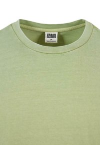 Svetlozelené tričko vyrobené z mäkkého materiálu s okrúhlym výstrihom. Štítok uvádza značku "Urban Classics" a veľkosť "M." Viditeľná je jemná štruktúra.