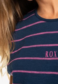 Marinrandig t-shirt med rosa horisontella ränder. Har rund halsringning och broderad "ROX"-logotyp i rosa på vänster sida.
