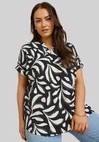 Blusa a maniche corte bianca e nera con un motivo a foglia, caratterizzata da scollo a V e maniche arrotolate, realizzata in tessuto testurizzato.
