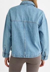 Lichtblauwe denimjas met een losse fit, lange mouwen en knoopmanchetten. Heeft een klassieke kraag en een rugnaaddetail.