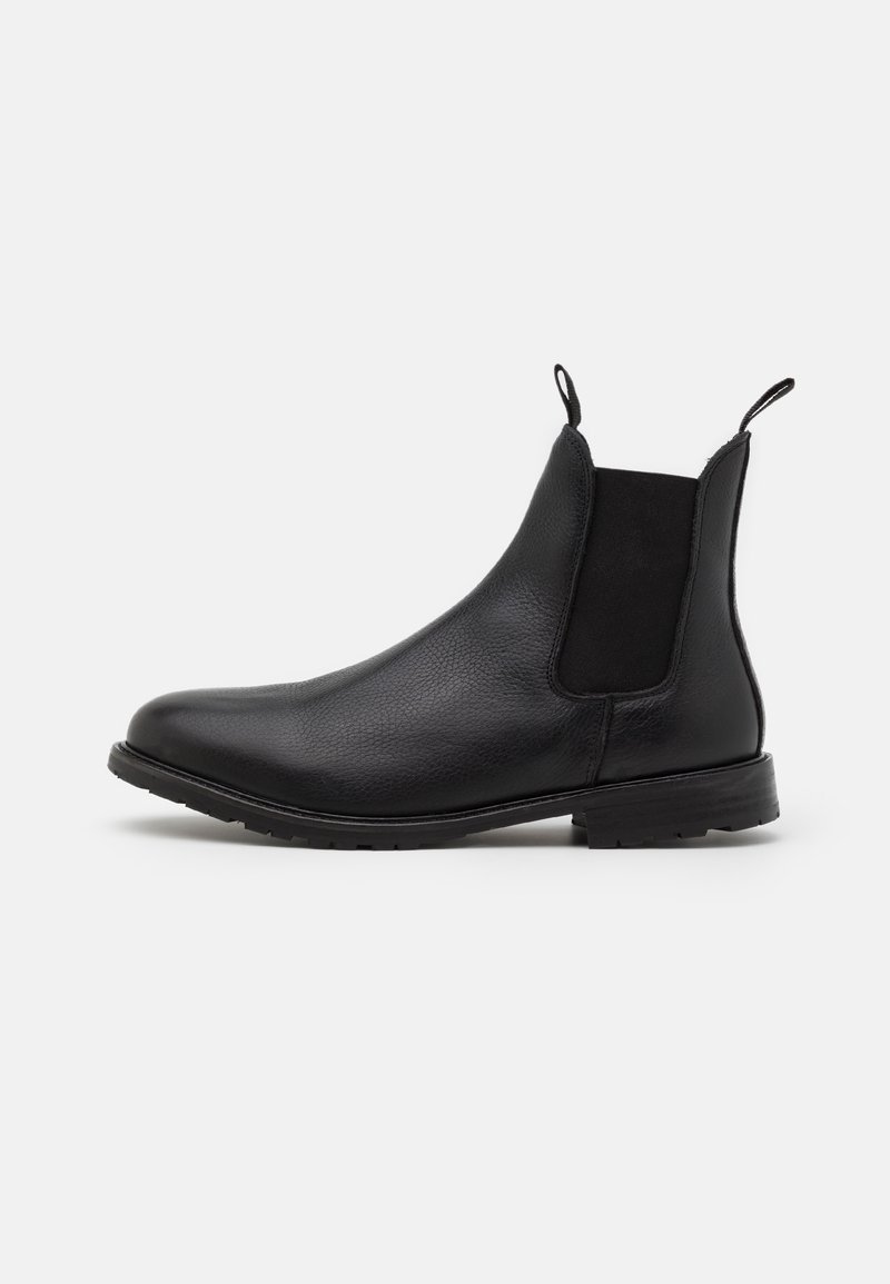 Bottes Chelsea en cuir noir avec panneaux latéraux élastiques, languettes à l'avant et à l'arrière, et talon bloc bas sur fond blanc.