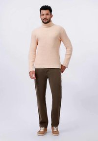 Sweter z golfem z dzianiny w jasnym brzoskwiniowym kolorze, o prążkowanej teksturze; zestawiony z oliwkowymi spodniami i brązowymi butami z białymi sznurówkami.