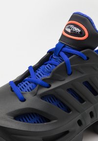 Baskets noires et bleues avec des lacets bleus, en tissu en maille respirant, et une languette rembourrée noire étiquetée "CLIMACOOL" avec une bordure orange.