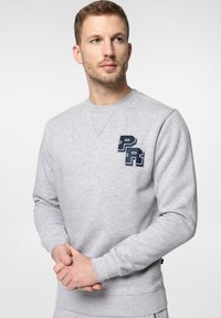 Szara bluza z okrągłym dekoltem, długimi rękawami, ściągaczami na rękawach i u dołu. Posiada niebieskie haftowane logo na lewej piersi. Miękka faktura materiału.