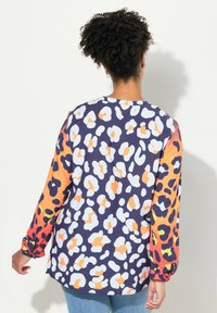 Maglietta a maniche lunghe in morbido tessuto con una base blu decorata con macchie di leopardo bianche e arancioni, e maniche arancioni sfumate con accenti verdi.