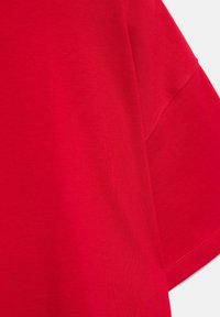 Tissu en coton rouge vif à manches courtes montrant une couture détaillée le long de la couture de l'épaule et de la manche.