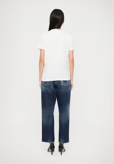 Maglietta bianca a maniche corte abbinata a jeans larghi in denim blu scuro. Scarpe con tacco alto nere, cuciture visibili e dettagli delle tasche sui jeans.