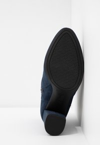 Semelle d'une bottine en daim bleu avec petit talon bloc, montrant une semelle extérieure noire texturée avec un design d'adhérence à motifs.