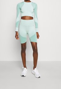 Mintgrünes Sport-Set mit einem kurvenlangen Langarmoberteil und hochgeschnittenen Shorts, die über strukturierte Muster und ein nahtloses Design verfügen.