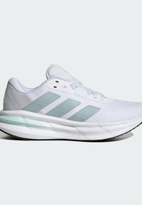 Bijela atletska cipela s mrežastim gornjištem, svijetlozelenim detaljima i tri pruge. Ima podstavljeni srednji sloj i teksturiranu potplat.