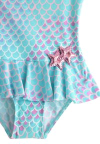 Un maillot de bain turquoise avec un motif écaille de couleur violette et rose, doté d'une jupe à volants et de deux accents étoilés brillants sur le côté.