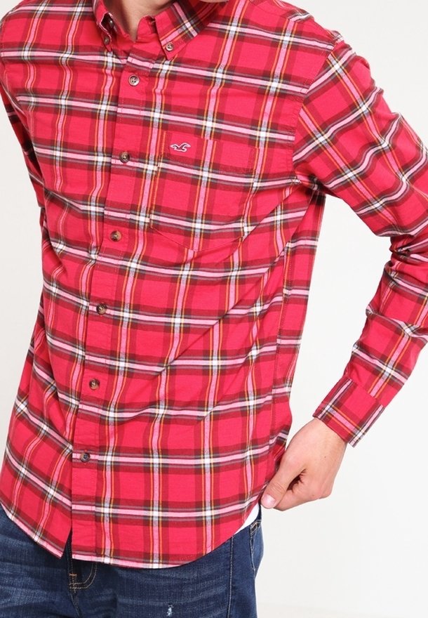 Chemise à carreaux rouge et noir à boutons, avec un col, arborant un petit logo et des boutons marron, associée à un jean en denim.