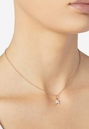 Gold chain necklace with a small white star-shaped pendant worn around a person's neck, near the collarbone.