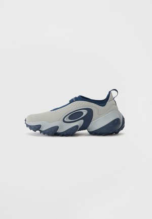 Cipele sivi gornji dio i mornarsko plave naglaske, karakterizira zakrivljeni dizajn, glatka tekstura i masivna potplat s plavom gumom s uzorkom.