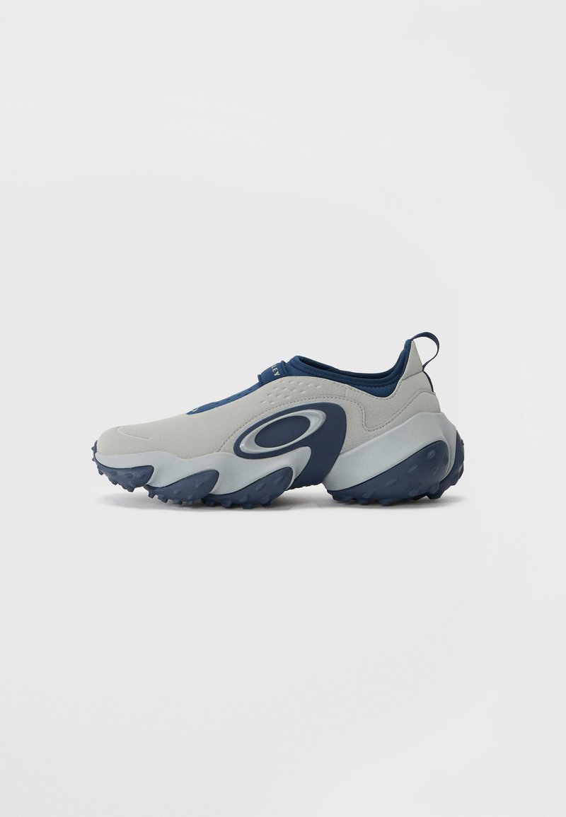 But z szarym wierzchem i granatowymi akcentami, charakteryzuje się zakrzywionym kształtem, gładką fakturą oraz masywną podeszwą z bieżnikowej niebieskiej gumy.