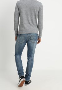 Harmaa pitkähihainen paita yhdistettynä sinisiin farkkuihin. Farkut ovat kapeat ja niissä on takataskuissa hillitty ompeleiden kuvio. Mustavalkoiset kengät.