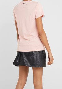 Světle růžové bavlněné tričko s kulatým výstřihem a krátkými rukávy, na zadní straně s malým černým logem "Karl Lagerfeld". V kombinaci s černou koženou sukní.