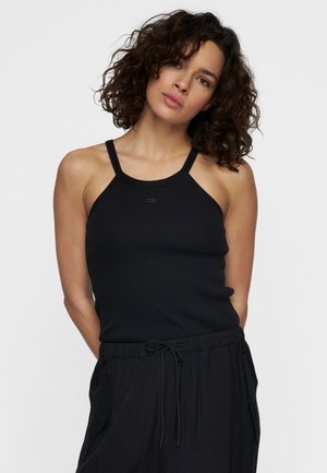 Black ribbed tank top with halter straps, featuring a fitted design and subtle stitching detail at the center front. Paired with black trousers.