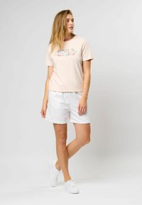 Lys rosa t-skjorte med blomstermønster, kombinert med hvite shorts og hvite joggesko. Korte ermer, avslappet passform, myk bomullstekstur.