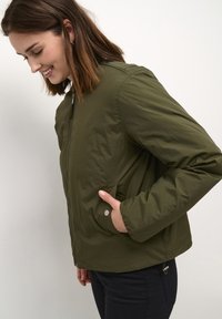 Olive rohe kergest bomber jope, mis on varustatud tõmblukuga eest, küljetaskutega ja ribatud mansettidega. Sile kangas, millel on veidi läikiv viimistlus.