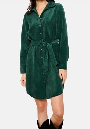 Grünes Cordkleid mit Knopfleiste, langen Ärmeln und passendem Gürtel in der Taille. Weiche Textur mit vertikalen Rillen.