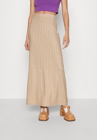 Glittrande beige maxikjol med vertikala ränder, tillverkad av strukturerad tyg. Kombineras med ljusbruna klumpiga klackskor.