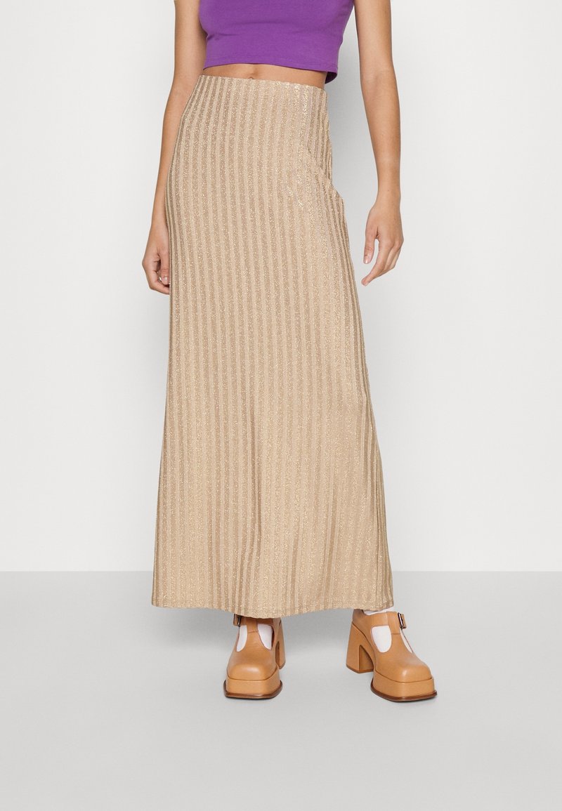 Glittrande beige maxikjol med vertikala ränder, tillverkad av strukturerad tyg. Kombineras med ljusbruna klumpiga klackskor.