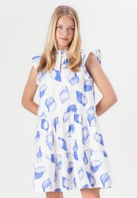 Valkoinen mekko, jossa on kerroksellinen muotoilu ja sinisen merisiilin kuvioita, lyhyillä röyhelösateilla ja etupuolella napitus yksityiskohtana kauluksessa.