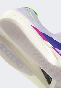 Gros plan sur la semelle d'une chaussure de course violette et blanche avec des accents bleus et roses, montrant la marque "ADIZERO" et une semelle texturée.
