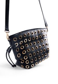Sac crossbody en cuir noir avec plusieurs œillets dorés, bandoulière réglable et fermeture zippée. Texture lisse.