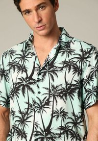 Korte mouwen shirt in een lichte muntkleur met een zwart palmbomenpatroon, met een kraag en een knopenvoorzijde. Zachte stofstructuur.