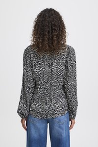 Blusa a righe in bianco e nero con maniche a sbuffo e schiena leggermente arricciata. Abbinata a jeans a gamba larga blu chiaro.