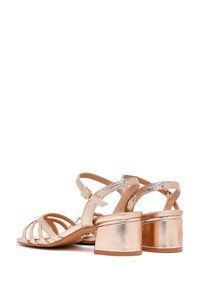 Sandali con tacco a blocco in oro rosa metallico, con design a strisce, caratterizzati da una finitura liscia e una fibbia alla caviglia regolabile per una vestibilità sicura.