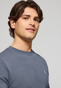 Grå sweatshirt med rund hals i bomullsblandning. Har en liten broderad logotyp på bröstet samt ribbade ärmslut och halsringning.