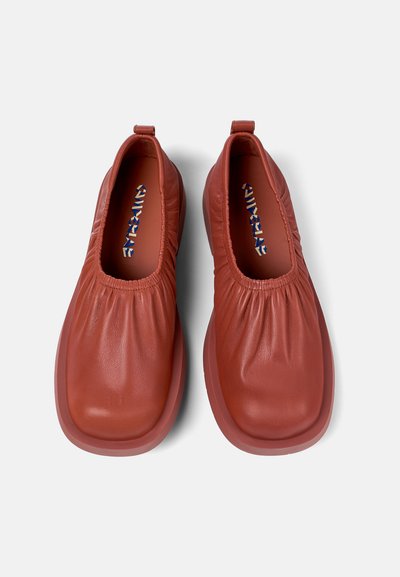 Red leather slip-on shoes with elasticated openings, rounded toes, and a thick rubber sole. Smooth texture with subtle gathering details.