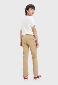Chino beige realizzati in cotone, design slim fit, con un'etichetta marrone sulla cintura posteriore e dettagli di cucitura bianca.