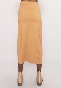 Persona vestida con una falda midi beige y botas de tobillo beige a juego, de pie contra un fondo claro y liso.