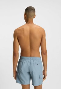 Costume da bagno azzurri chiari con elastico in vita e una tasca posteriore. Texture liscia, lunghezza sopra il ginocchio e design minimalista.