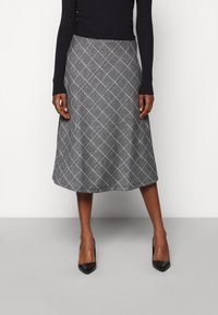 A-siluetová sukně s černobílým kostkovaným vzorem, vyrobená z texturované látky, s délkou po kolena a jemným leskem, doplněná černými lodičkami.