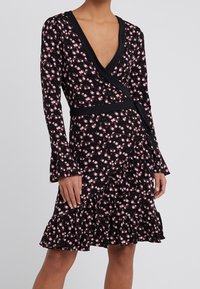 Musta kukkamekko pitkillä hihoilla, V-pääntiellä ja levenevällä helmalla. Omistaa kietaisusuunnittelun, vaaleanpunaiset kukkakuviot ja röyhelödetailin hameessa.