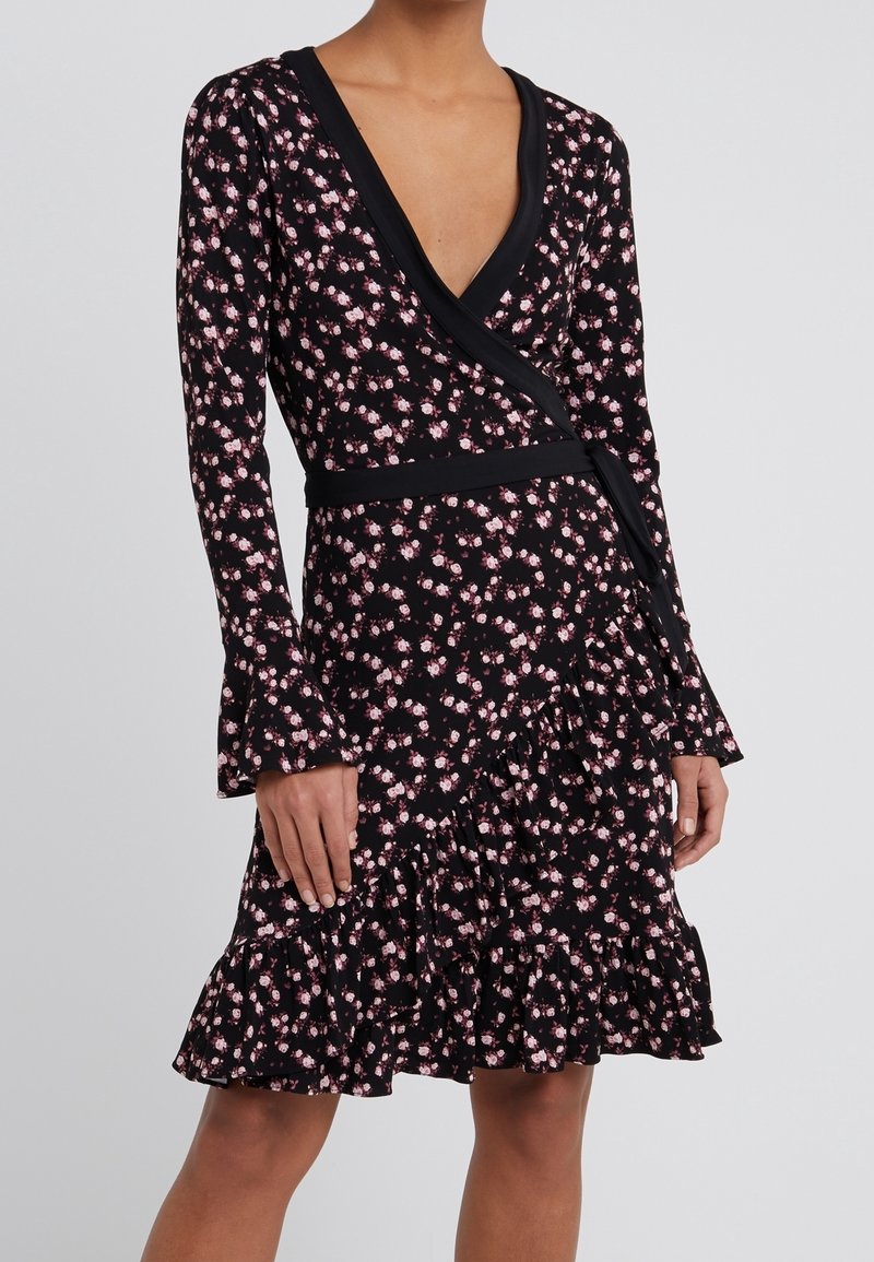 Musta kukkamekko pitkillä hihoilla, V-pääntiellä ja levenevällä helmalla. Omistaa kietaisusuunnittelun, vaaleanpunaiset kukkakuviot ja röyhelödetailin hameessa.