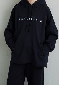 Felpa oversize nera realizzata in tessuto morbido con tasca a marsupio, che presenta la scritta "MARGIELA 6" in caratteri bianchi sul davanti.
