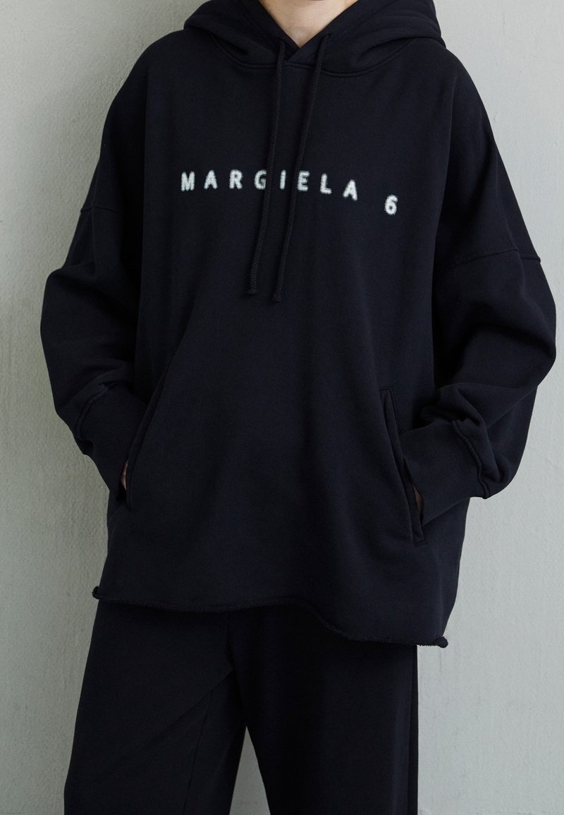 Felpa oversize nera realizzata in tessuto morbido con tasca a marsupio, che presenta la scritta "MARGIELA 6" in caratteri bianchi sul davanti.